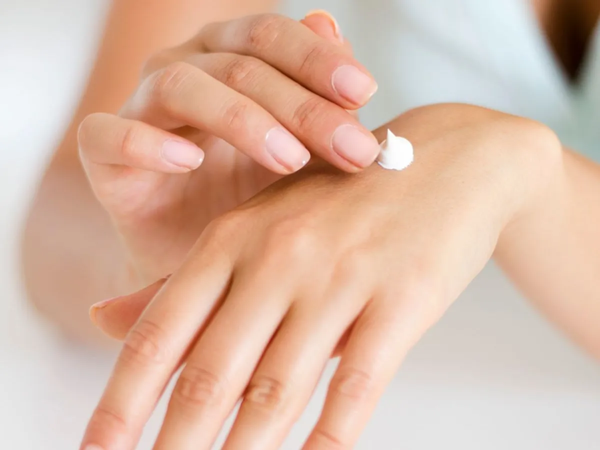 Mujer extendiendo crema hidratante con los dedos sobre el dorso de la otra mano