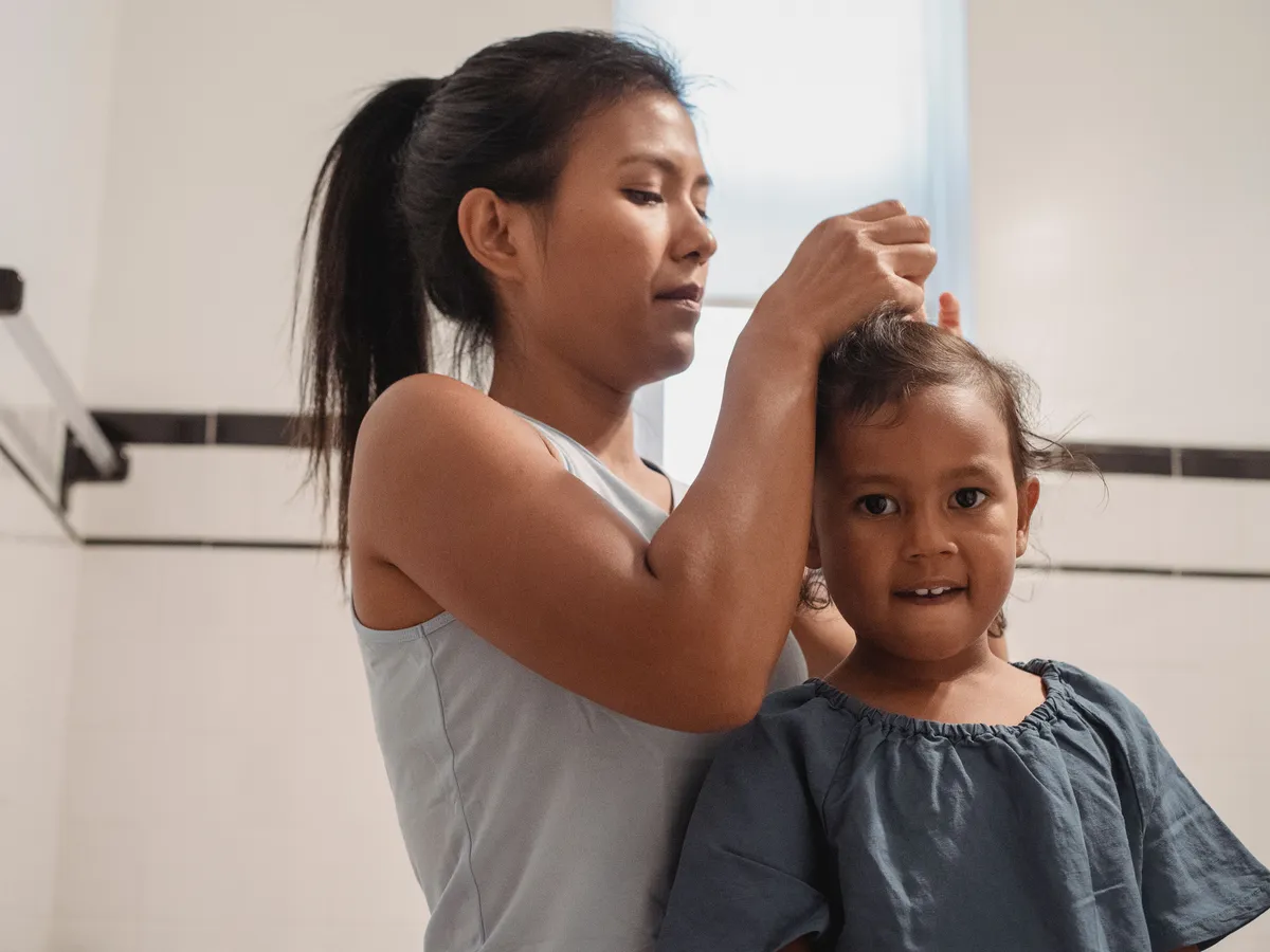 Madre revisando de cerca el cuero cabelludo de su hija en casa